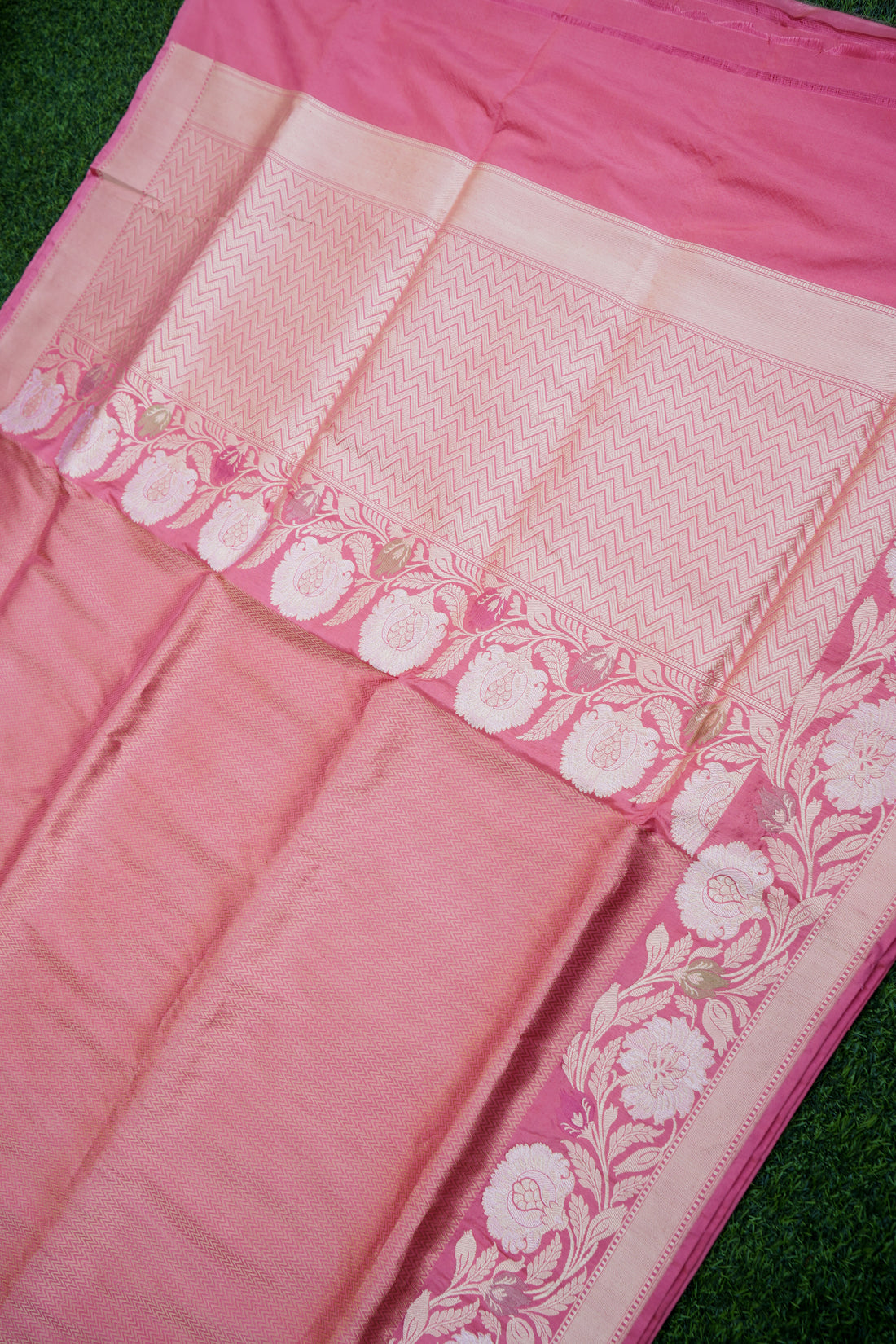 Close-up of a pink saree with white floral patterns on a green background