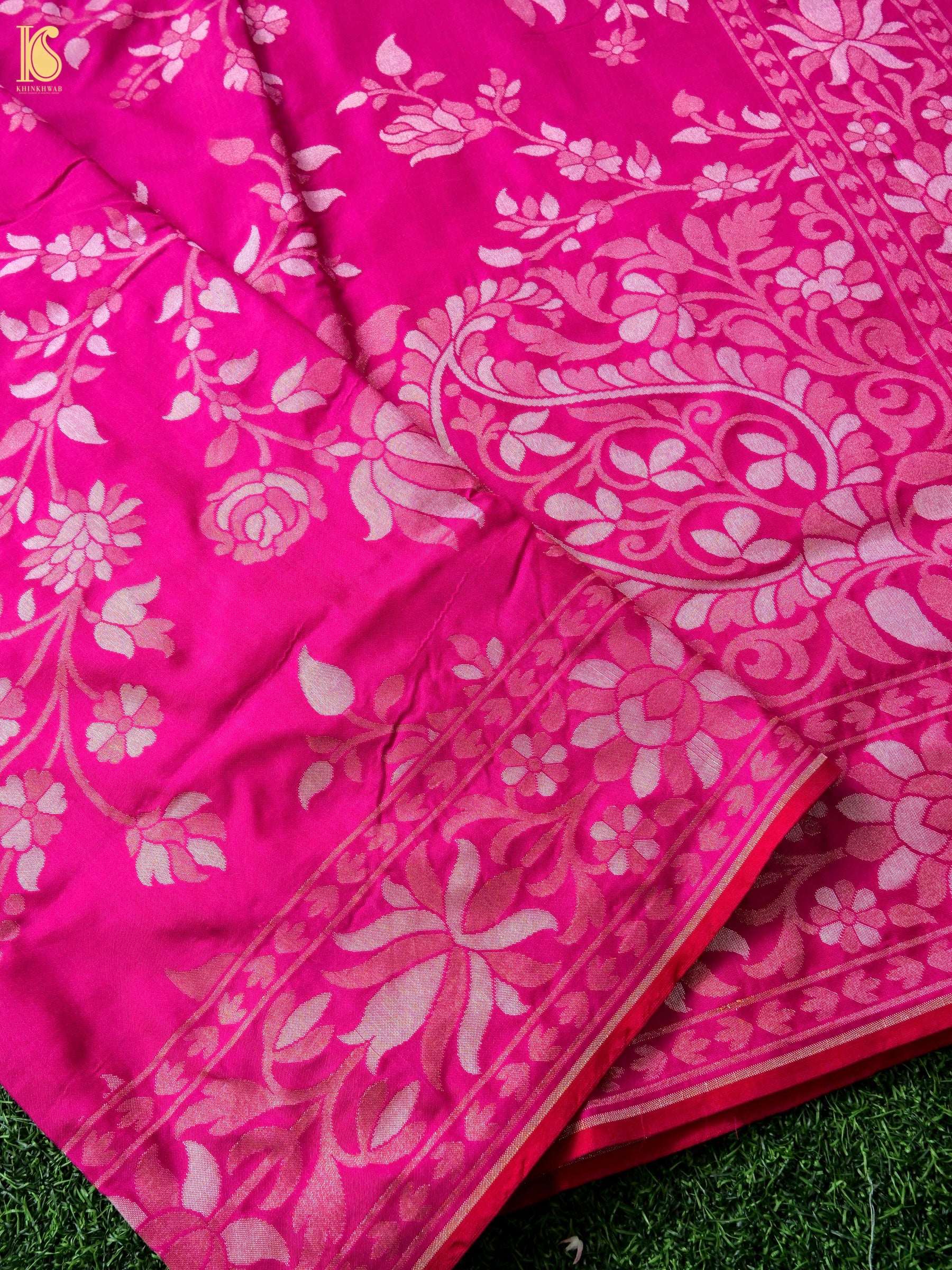 A close-up of a bright pink fabric with a light pink floral and paisley pattern, draped over green grass.