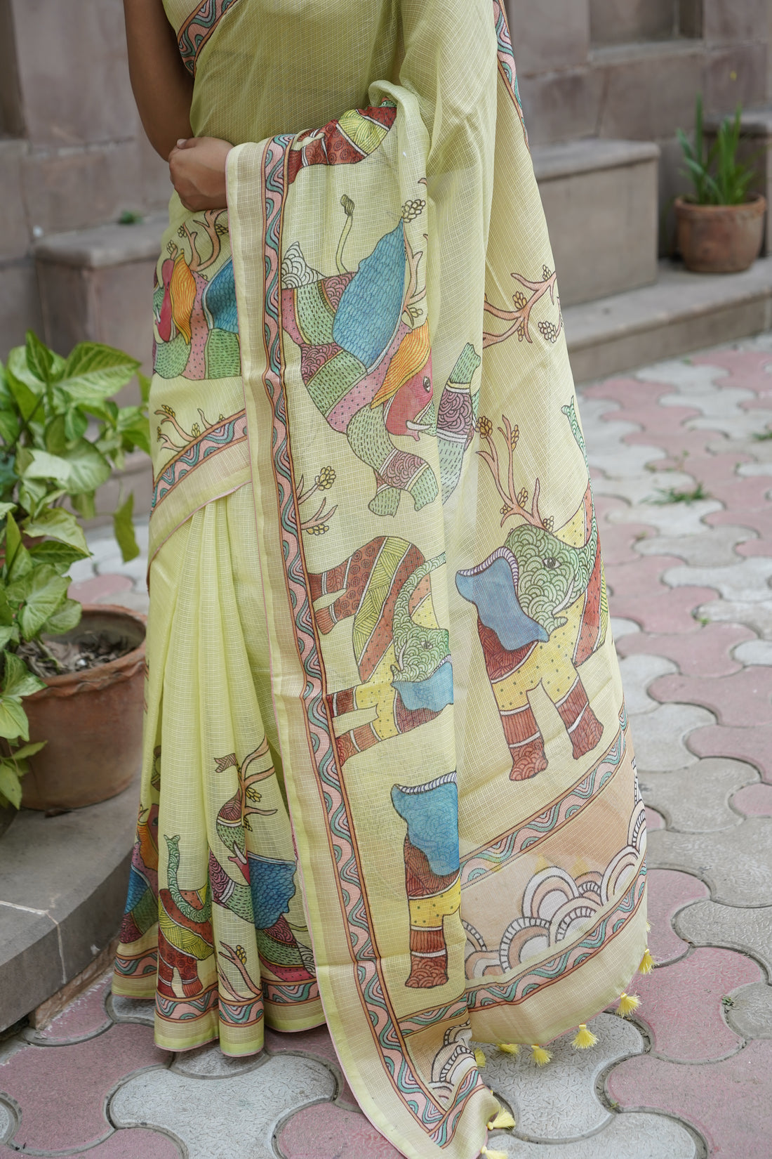 Person wearing a light green saree with colorful elephant patterns on a stone pathway.