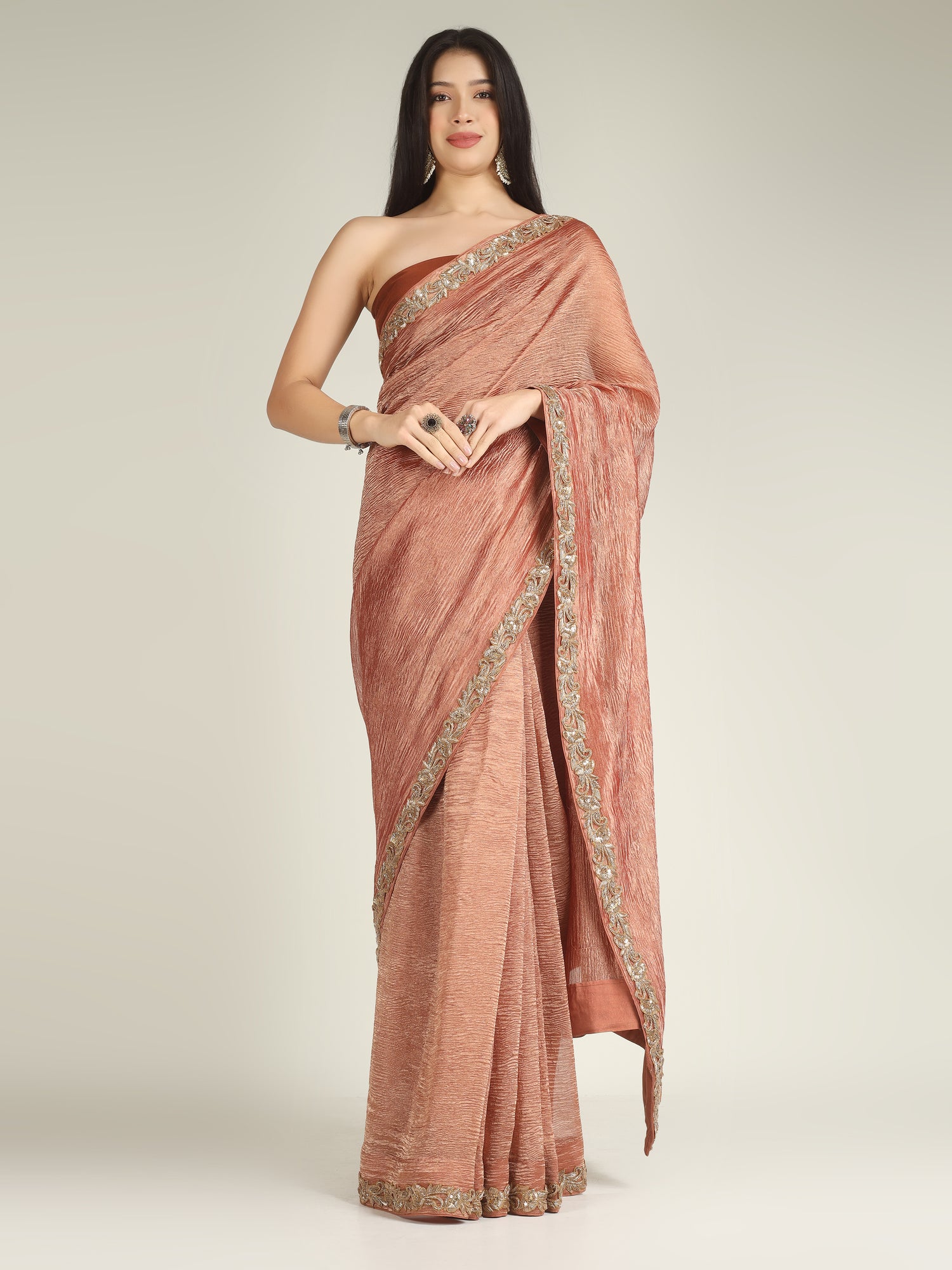 Woman wearing a rust-colored saree with gold border on a light gray background
