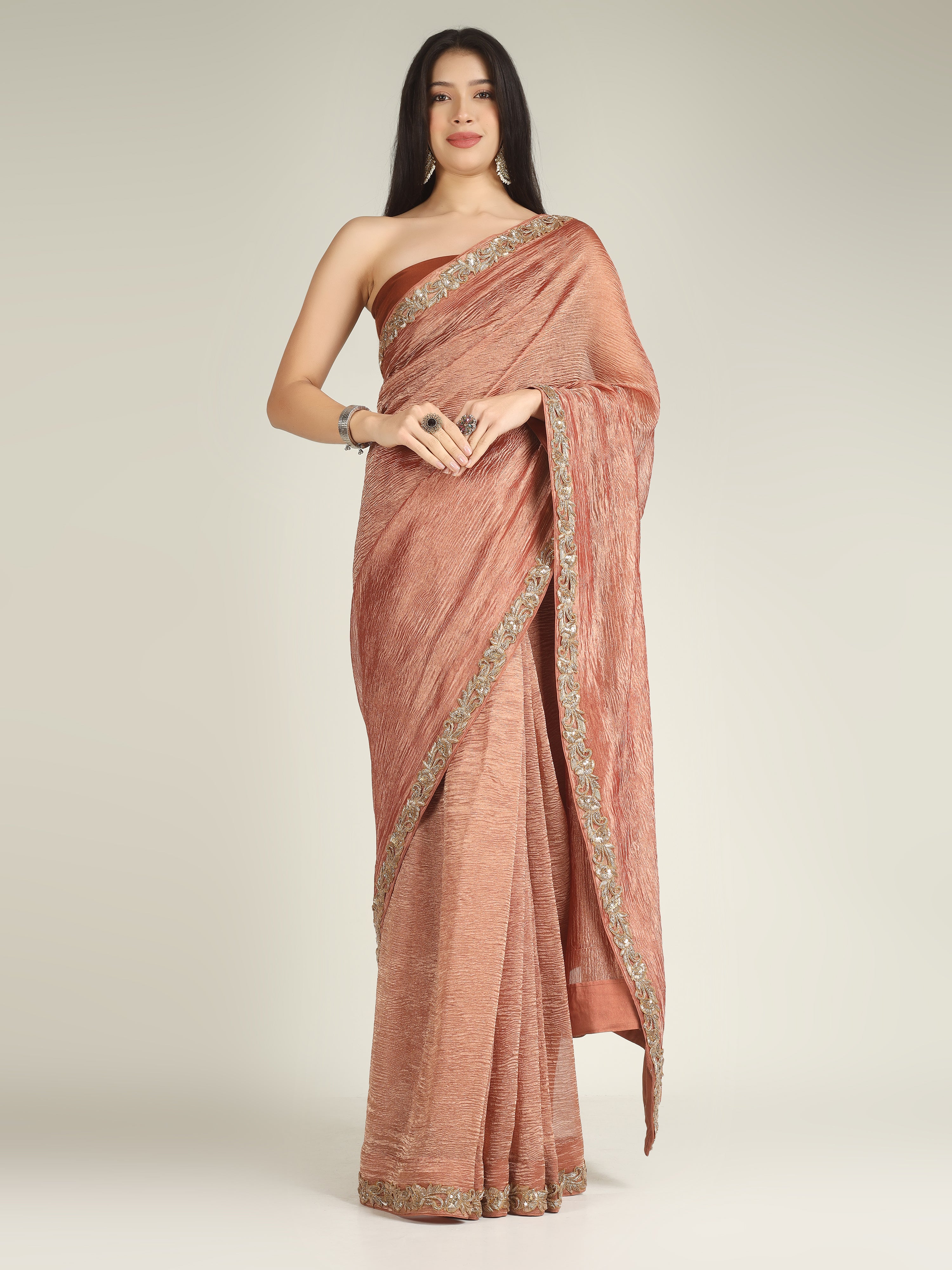 Woman wearing a rust-colored saree with gold border on a light gray background