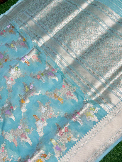 Blue saree with floral patterns and silver border on a green background
