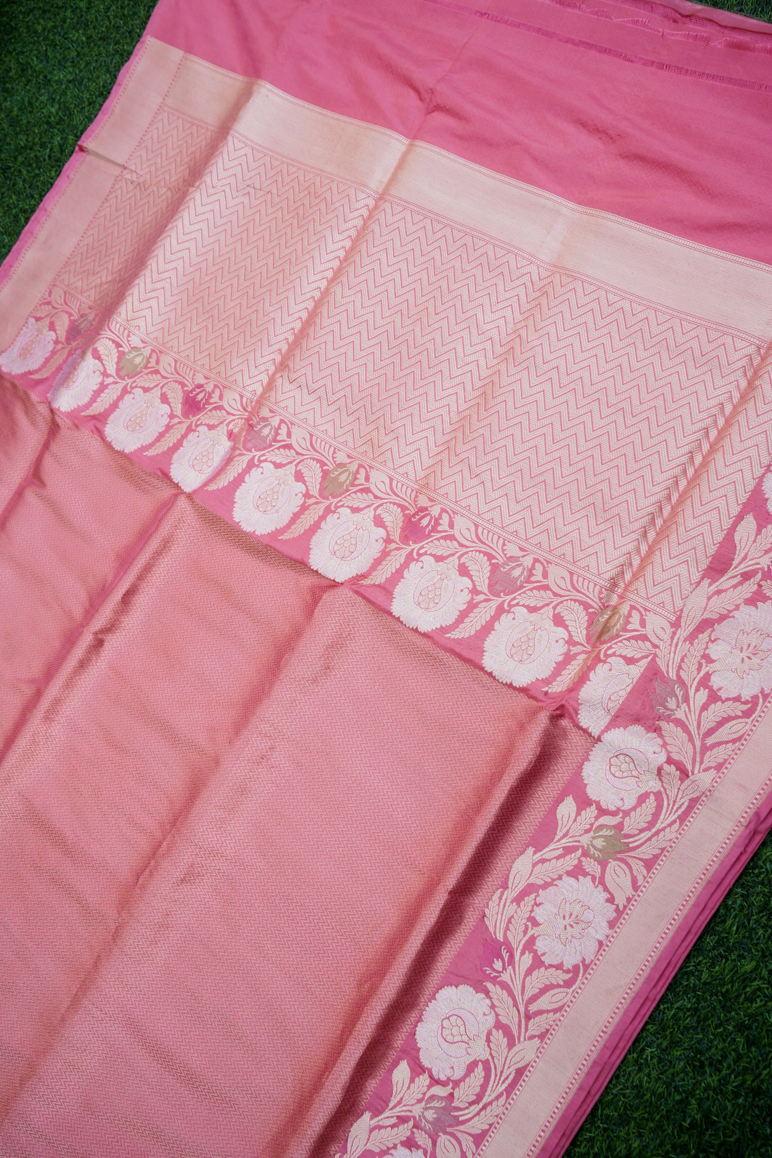 Close-up of a pink saree with white floral patterns on a green background