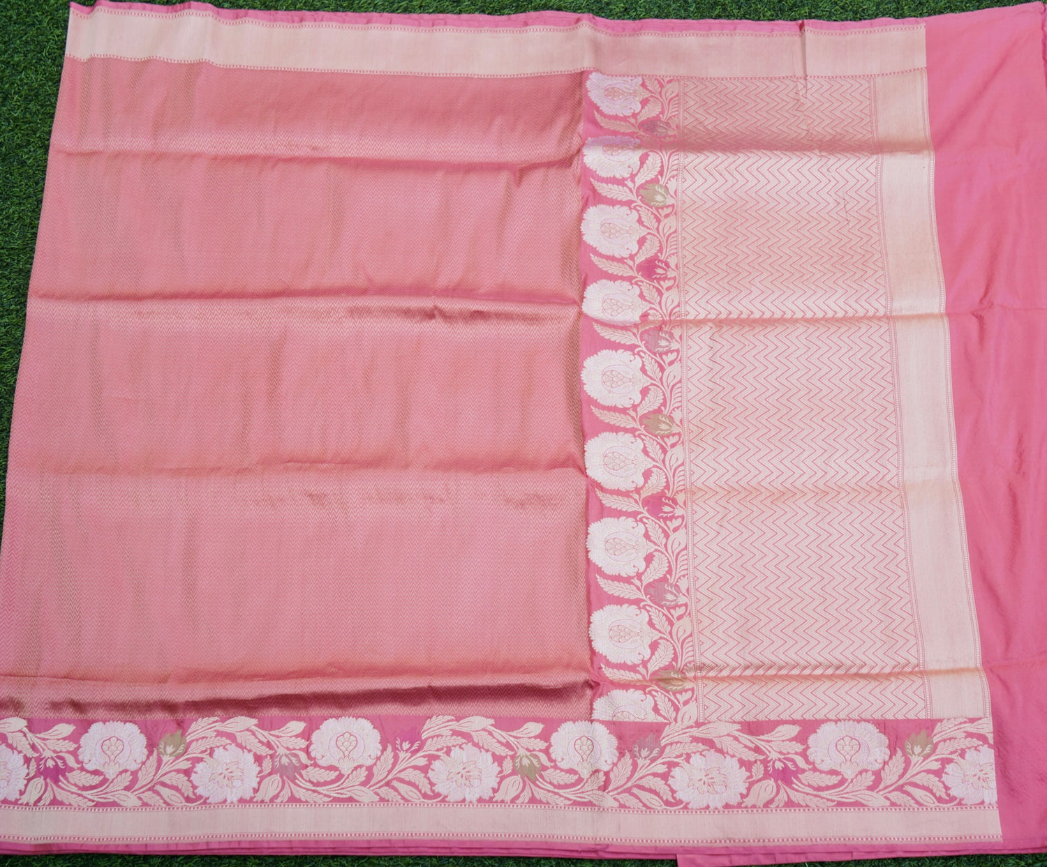 Pink saree with white floral border on a green background