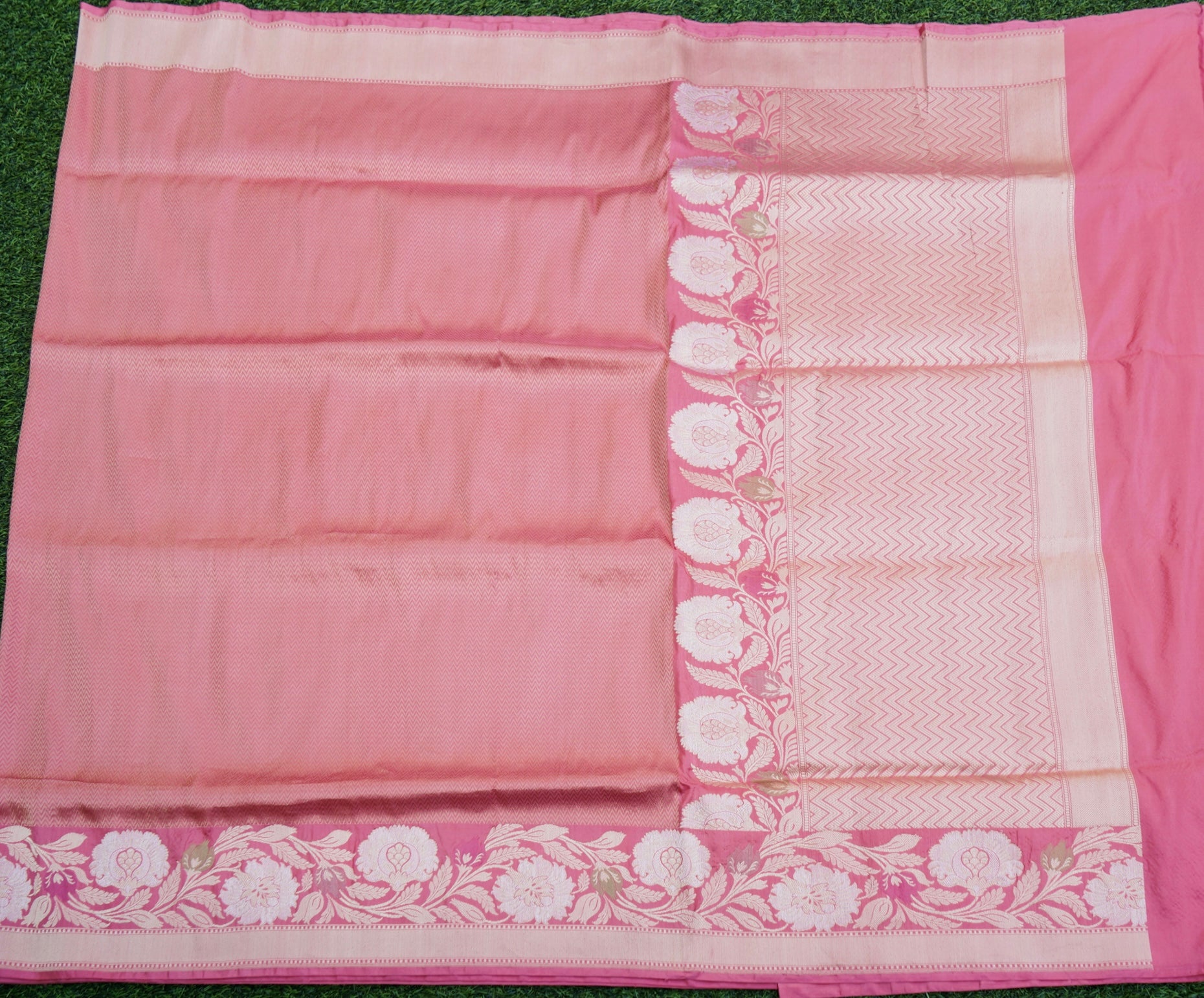 Pink saree with white floral border on a green background