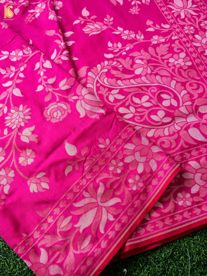 A close-up of a bright pink fabric with a light pink floral and paisley pattern, draped over green grass.